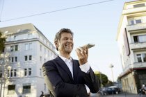 Sorridente uomo d'affari maturo utilizzando smartphone in città — Foto stock