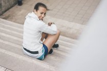 Смолящая спортивная молодая женщина, сидящая на лестнице снаружи — стоковое фото