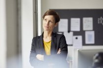 Attractive businesswoman standing in office with arms crossed — Stock Photo