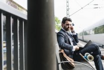 Empresario con monopatín, laptop y auriculares en la plataforma - foto de stock