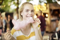 Portrait of young woman eating pink candy floss on streetfood festival — Stock Photo