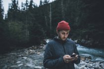 Canadá, Columbia Británica, Parque Nacional Glaciar, hombre con teléfono celular en Illecillewaet River en el bosque - foto de stock