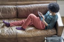 Young woman lying on couch and using tablet — Stock Photo