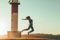 Young woman jumping in desert landscape at lighthouse — Stock Photo