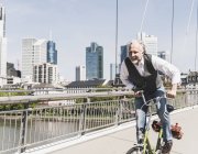 Feliz hombre maduro en bicicleta cruzando el puente en la ciudad - foto de stock