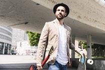 Young man with guitar and skateboard walking in the city — Stock Photo
