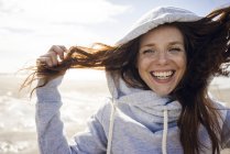 Frau amüsiert sich an einem windigen Strand, trägt Kapuze — Stockfoto