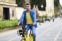 Jovem montando bicicleta de aluguel na cidade — Fotografia de Stock