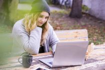 Portrait of smiling young woman with laptop skyping outdoors in autumn — Stock Photo