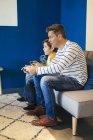 Father and son playing video game on couch at home — Stock Photo
