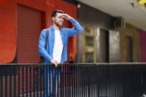 Young man standing in the city, looking at distance, shielding eyes — Stock Photo
