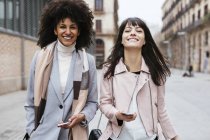 Espagne, Barcelone, portrait de deux amies avec des téléphones portables marchant en ville — Photo de stock