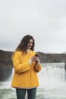 Islande, femme avec téléphone portable à la cascade Godafoss — Photo de stock