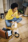 Giovane donna afroamericana seduta vicino al giradischi, che controlla lo smartphone mentre mangia tagliatelle a casa — Foto stock