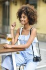 Portrait of fashionable young woman with camera drinking beer outdoors — Stock Photo