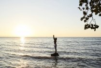 Junge Frau praktiziert Yoga auf einem Felsen im Meer bei Sonnenuntergang — Stockfoto