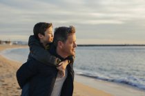 Father giving piggyback to son on beach at sunset — Stock Photo