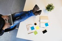 Cropped image of businessman using laptop with feet on desk in office — Stock Photo