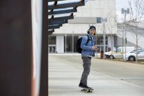 Young man skateboarding in the city, using smartphone, listening music — Stock Photo