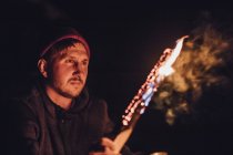 Homme tenant une bûche brûlante la nuit — Photo de stock