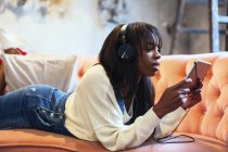 Young woman lying on the couch using tablet and headphones — Stock Photo