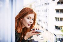 Портрет рыжеволосой женщины на телефоне, высунутой в окно — стоковое фото