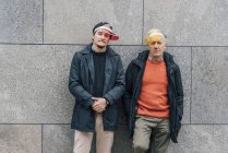 Портрет молодого чоловіка і старшого чоловіка, що носить сонячні козирки, спираючись на стіну — стокове фото