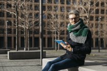 Uomo d'affari con tablet seduto sulla panchina in città in inverno — Foto stock