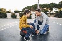 Vater schnürt Sohn Schuh auf Basketballfeld — Stockfoto