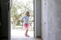 Portrait de petite fille riante debout devant la porte d'entrée ouverte — Photo de stock