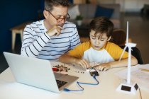 Vater und Sohn beim Zusammenbau eines Bausatzes mit Laptop und Windkraftmodell — Stockfoto
