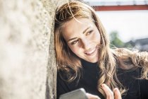 Ritratto di donna sorridente con smartphone appoggiato al muro — Foto stock