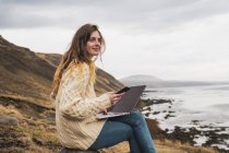 Islande, femme utilisant un ordinateur portable et un téléphone portable sur la côte — Photo de stock