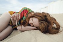 Mulher ruiva deitada na praia, com areia passando pela mão — Fotografia de Stock