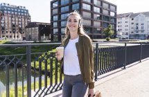 Junge Frau läuft auf Brücke, trinkt Kaffee, hört Musik mit Kopfhörern — Stockfoto