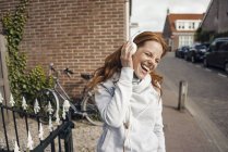 Femme rousse utilisant un casque dans la ville — Photo de stock