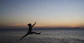 Mujer joven saltando al mar al atardecer - foto de stock