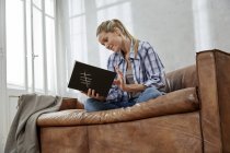 Donna sorridente seduta sul divano con libro — Foto stock