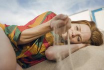 Mulher ruiva deitada na praia, com areia passando pela mão — Fotografia de Stock