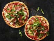 Two Pizzas with ham and rocket on dark ground — Stock Photo