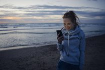 Mulher usando smartphone na praia ao pôr do sol — Fotografia de Stock