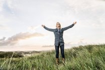Donna felice in piedi in dune con le braccia alzate — Foto stock