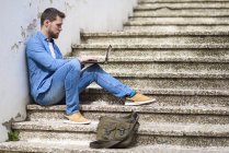 Giovane seduto sulle scale, al lavoro, utilizzando il computer portatile — Foto stock
