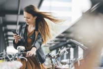 Young woman with bicycle using cell phone in the city — Stock Photo