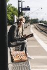 Молодая женщина, сидящая на вокзале, используя цифровой планшет — стоковое фото