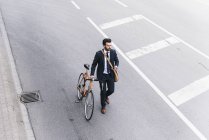 Uomo d'affari con bicicletta e cellulare che cammina per strada — Foto stock