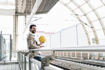 Усміхнений молодий чоловік з мобільним телефоном і баскетболом на платформі станції — стокове фото