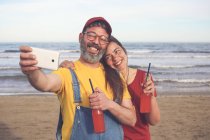 Couple with soft drinks taking selfie with smartphone on the beach — Stock Photo