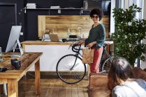Young woman with bicycle arriving in modern office — Stock Photo