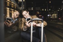 Uomo d'affari sorridente che usa il cellulare alla stazione del tram di notte — Foto stock